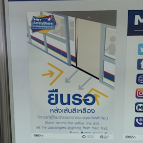 A safety poster featuring an illustration of a train platform with passengers inside a train. Arrows guide commuters to stand behind the yellow line. The poster includes both Thai and English text, emphasizing safety instructions for standing back until passengers have disembarked from the train.