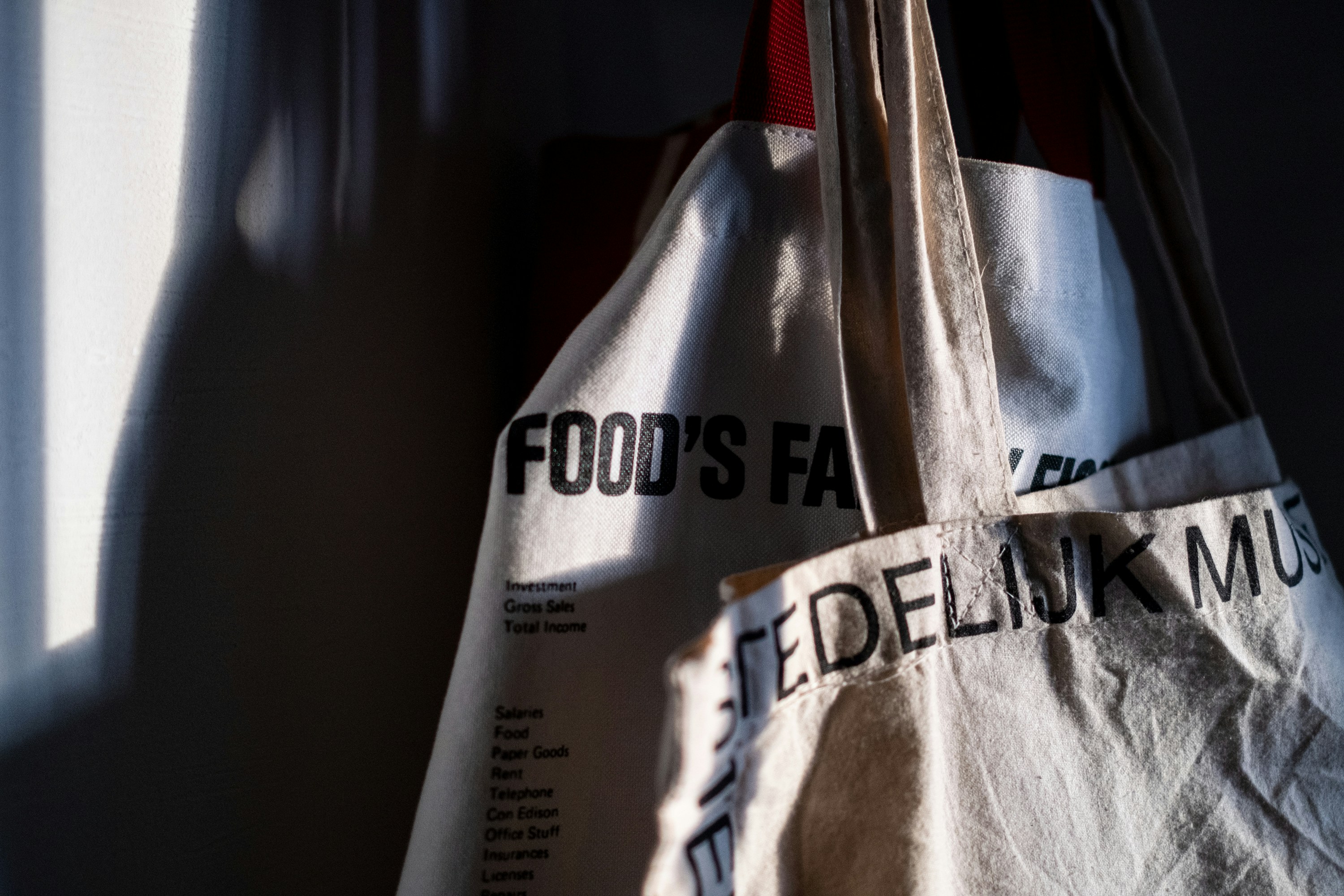 Black canvas tote bag on dark textured surface, dramatic side lighting with minimal branding visible