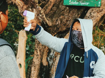A health outreach nurse gently checking a child's heartbeat under a large tree.