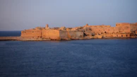 Sunset over the historic Forte São Mateus with golden light reflecting on calm waters.