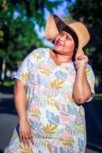 A cheerful young woman wearing a colorful printed dress, smiling in a sunlit urban setting.