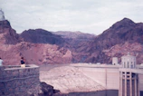 A panoramic view of a large hydroelectric dam under construction surrounded by mountains.
