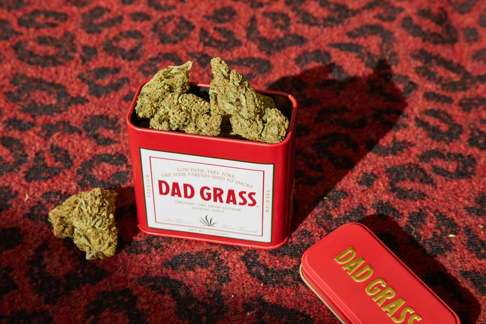 a tin of dad grass next to a tin of buds