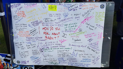 A board filled with various handwritten messages expressing opinions about Brexit. People have used different colors to write their thoughts, which range from humorous and sarcastic remarks to serious political statements. The board acts as a public platform for opinions on the topic.
