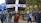 A group of people are participating in a public march or protest, walking along a path lined with trees. One person is holding a large black flag with a white cross and the words 'one and all for Europe' written in bold letters. Other individuals are carrying EU flags with yellow stars on a blue background. The participants are dressed in casual attire, some with badges or stickers indicating their support for Europe.
