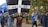 A group of people are participating in a public march or protest, walking along a path lined with trees. One person is holding a large black flag with a white cross and the words 'one and all for Europe' written in bold letters. Other individuals are carrying EU flags with yellow stars on a blue background. The participants are dressed in casual attire, some with badges or stickers indicating their support for Europe.