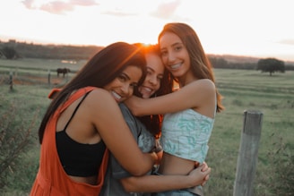 three girls hugging each other in a field