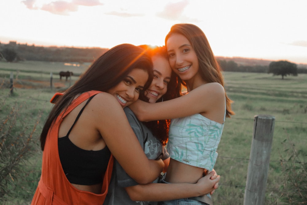 three girls hugging each other in a field
