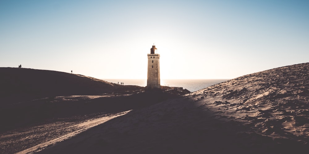 a lighthouse on top of a hill with the sun in the background