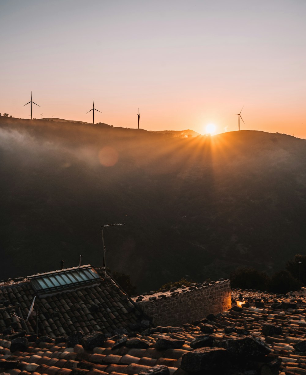 the sun is setting over a mountain with windmills in the background