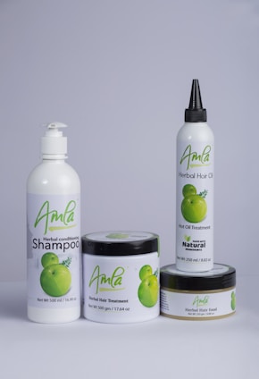 A set of four hair care products with white packaging, each featuring the word 'Amla' and an image of green fruit. The products include a herbal conditioning shampoo, herbal hair treatment, herbal hair oil, and herbal hair food.
