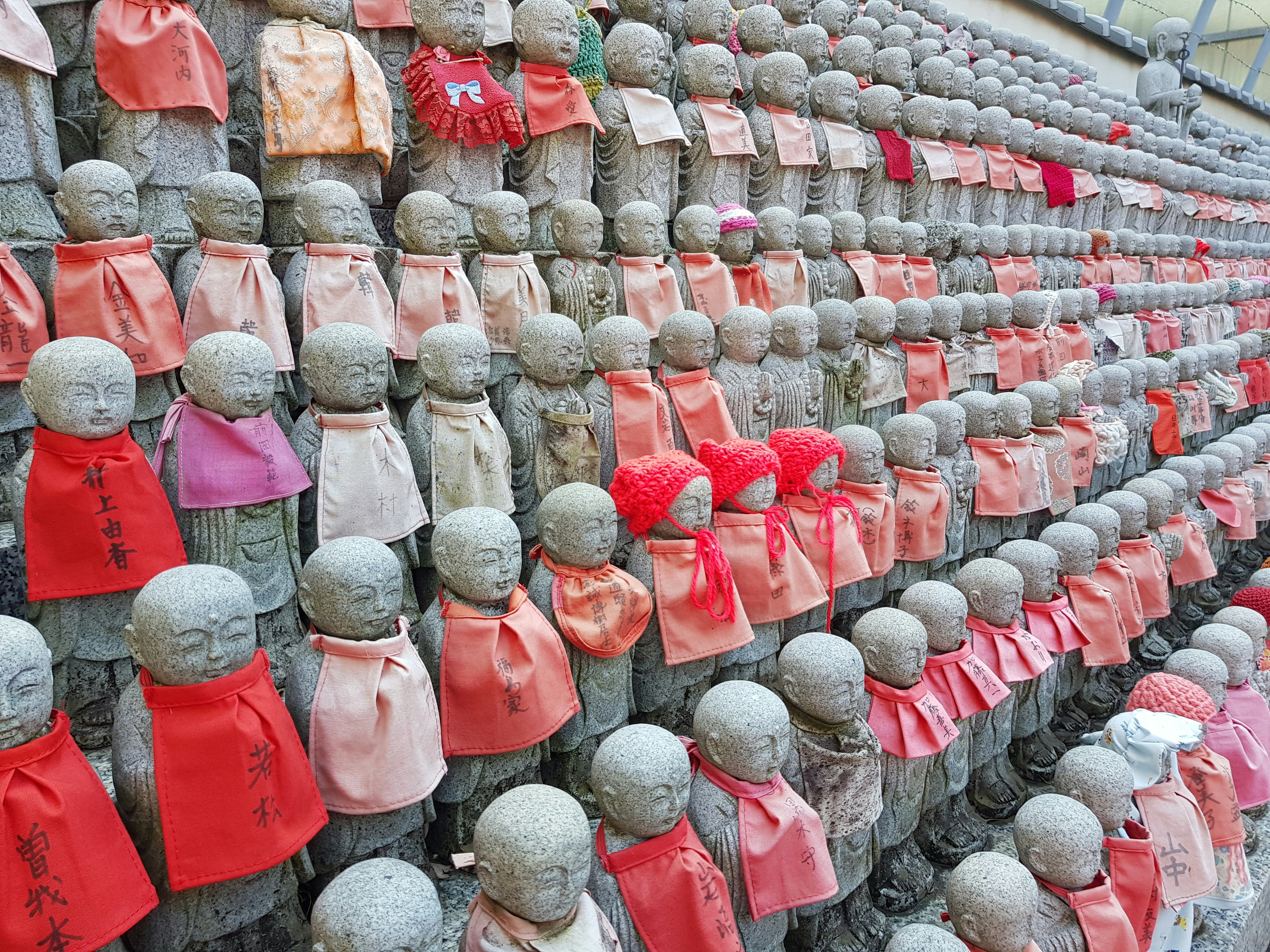 a wall of statues with red and pink scarves on them