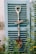 A decorative shovel with flowers and a 'Garden' sign hanging against a rustic, light blue shutter. Surrounding greenery adds a touch of nature to the scene.