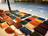 A display of various leather wallets arranged on a table, featuring different colors and styles. The table is situated outdoors with a tiled ground in the background.