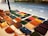 A display of various leather wallets arranged on a table, featuring different colors and styles. The table is situated outdoors with a tiled ground in the background.