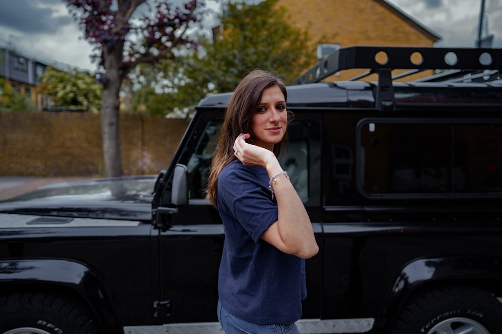 uma mulher em pé na frente de um land rover preto