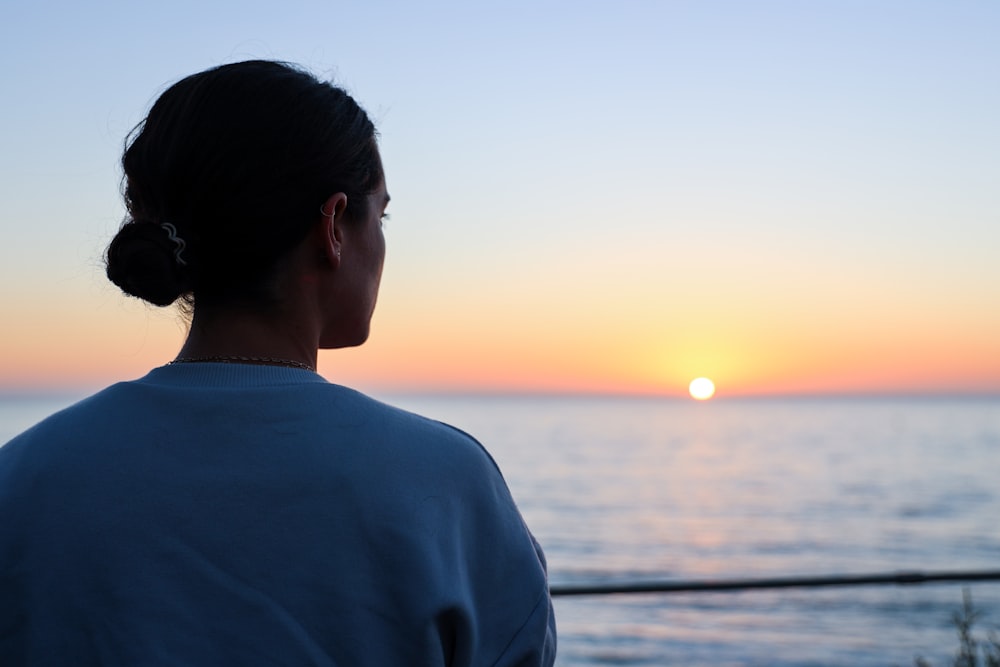 a woman looking out at the ocean at sunset