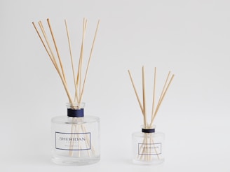 two bottles with reeds in them on a white surface