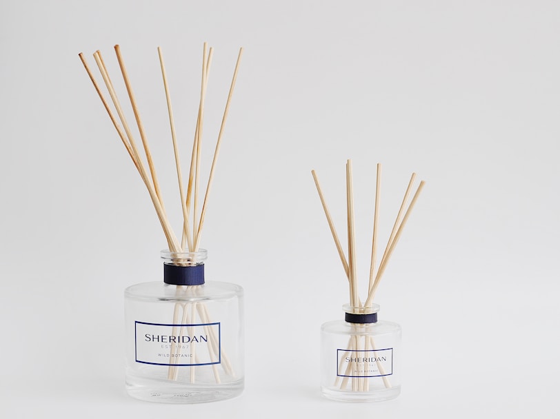 two bottles with reeds in them on a white surface