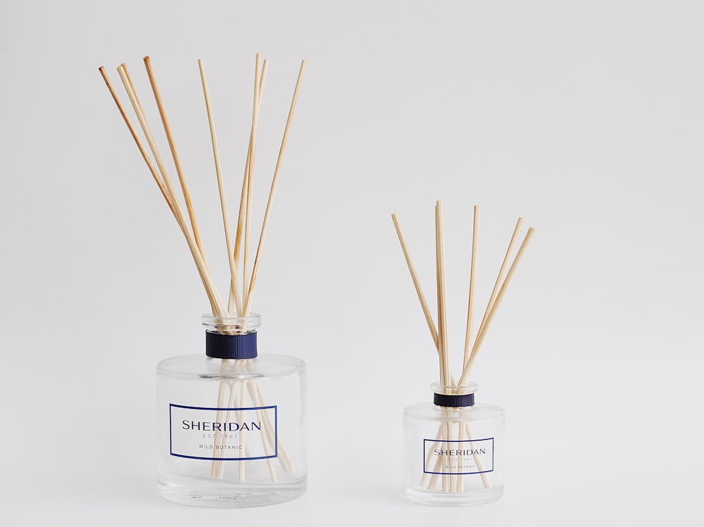 two bottles with reeds in them on a white surface