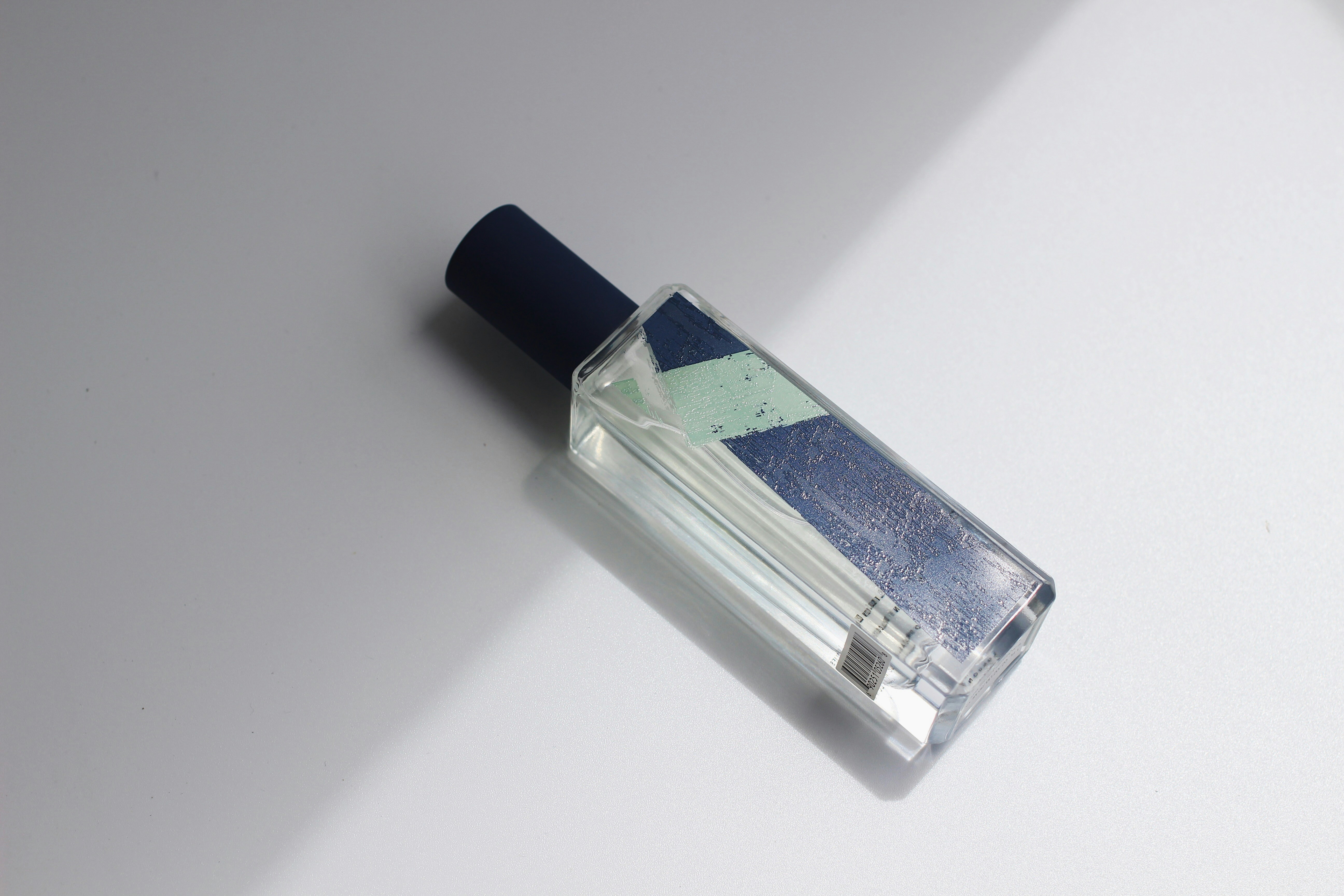 Minimalist clear glass perfume bottle with green-tinted liquid on light stone surface with botanicals