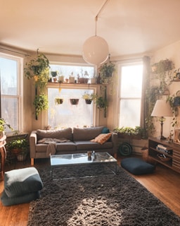 A cozy living room featuring modern furniture, plants, and natural light streaming through large windows.