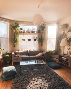A cozy living room featuring modern furniture, plants, and natural light streaming through large windows.