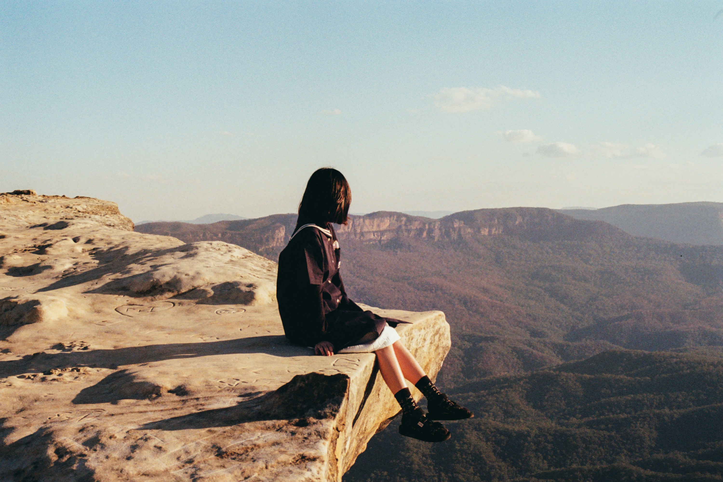 a woman sitting on top of a cliff overlooking a valley
