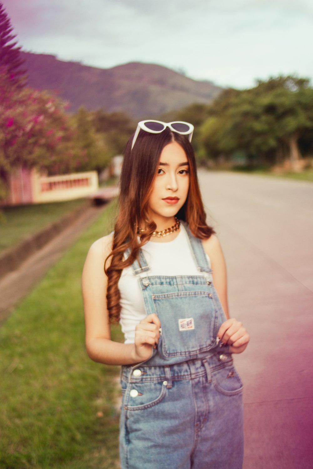 a woman in overalls and sunglasses standing on the side of a road