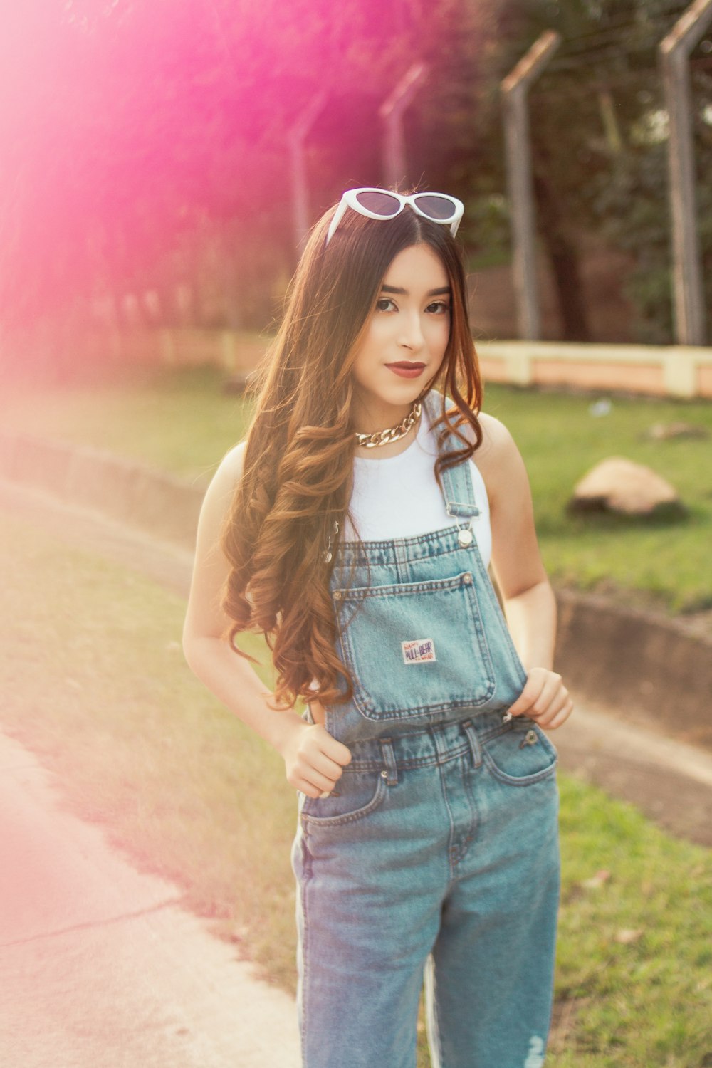 a woman in overalls and sunglasses standing on the side of a road