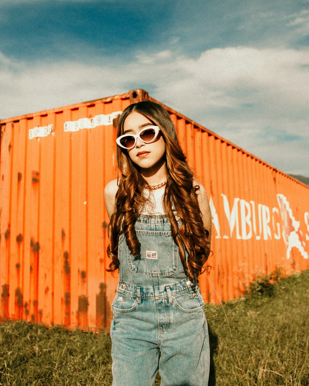 a girl in overalls standing in front of an orange building