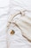 A wooden hanger holds a beige linen garment, laid out on a soft white surface, next to a yellow pacifier with a gray rim.