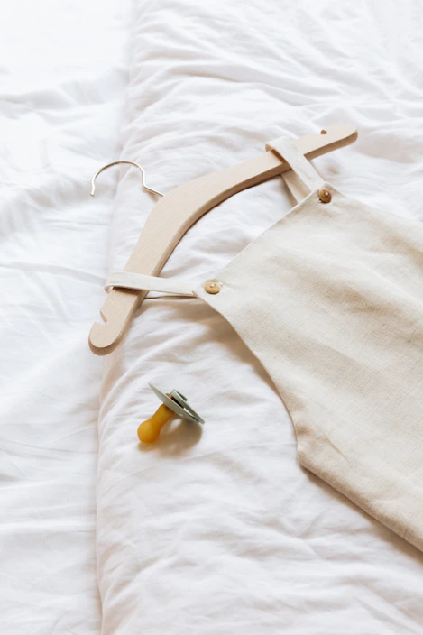 Soft pastel-hued baby clothes neatly arranged on a wooden hanger.