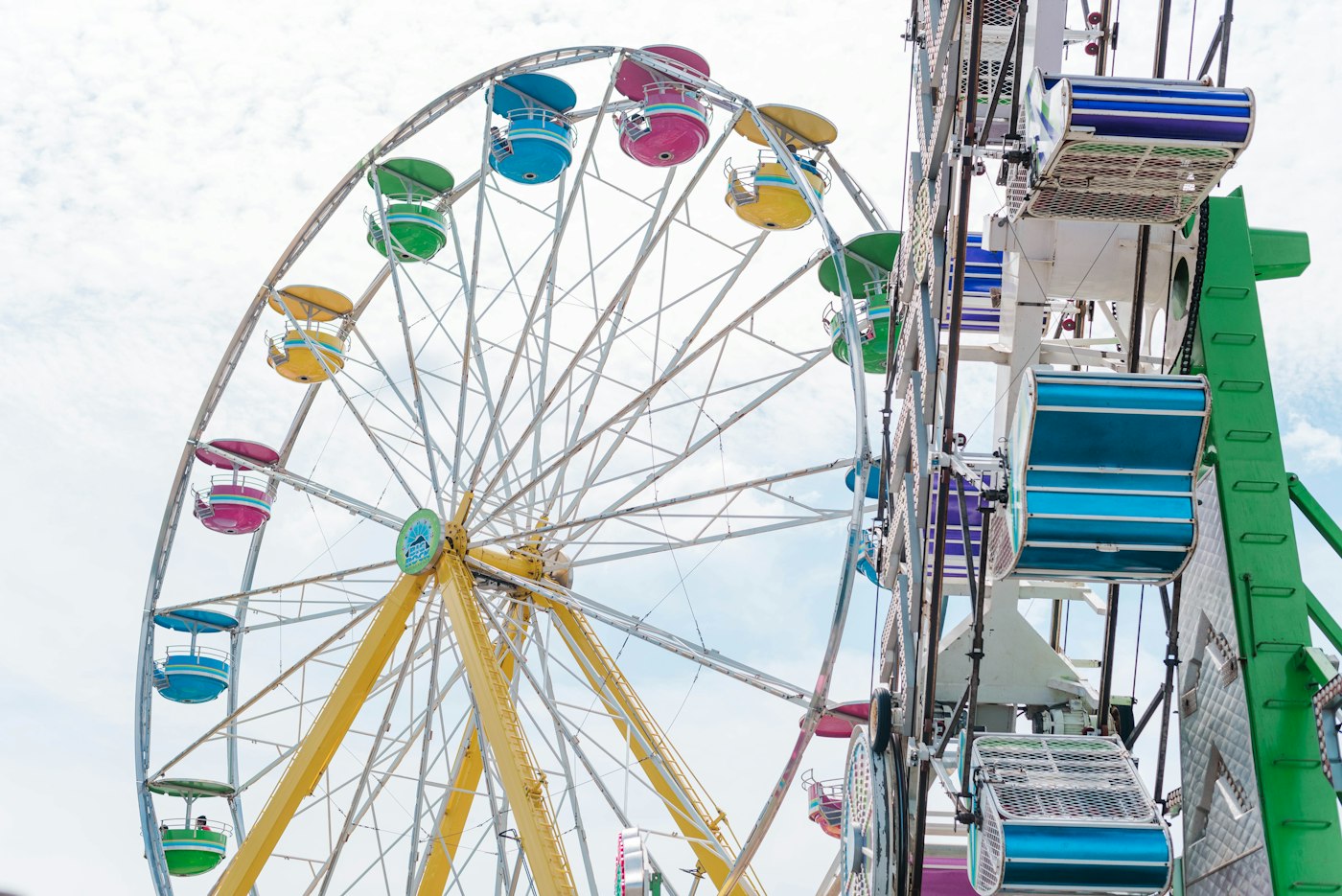 A Ferris wheel with pastel gondolas turning beside a midway ride under a cloudy sky, the classic sight at New Hampshire fall fairs
