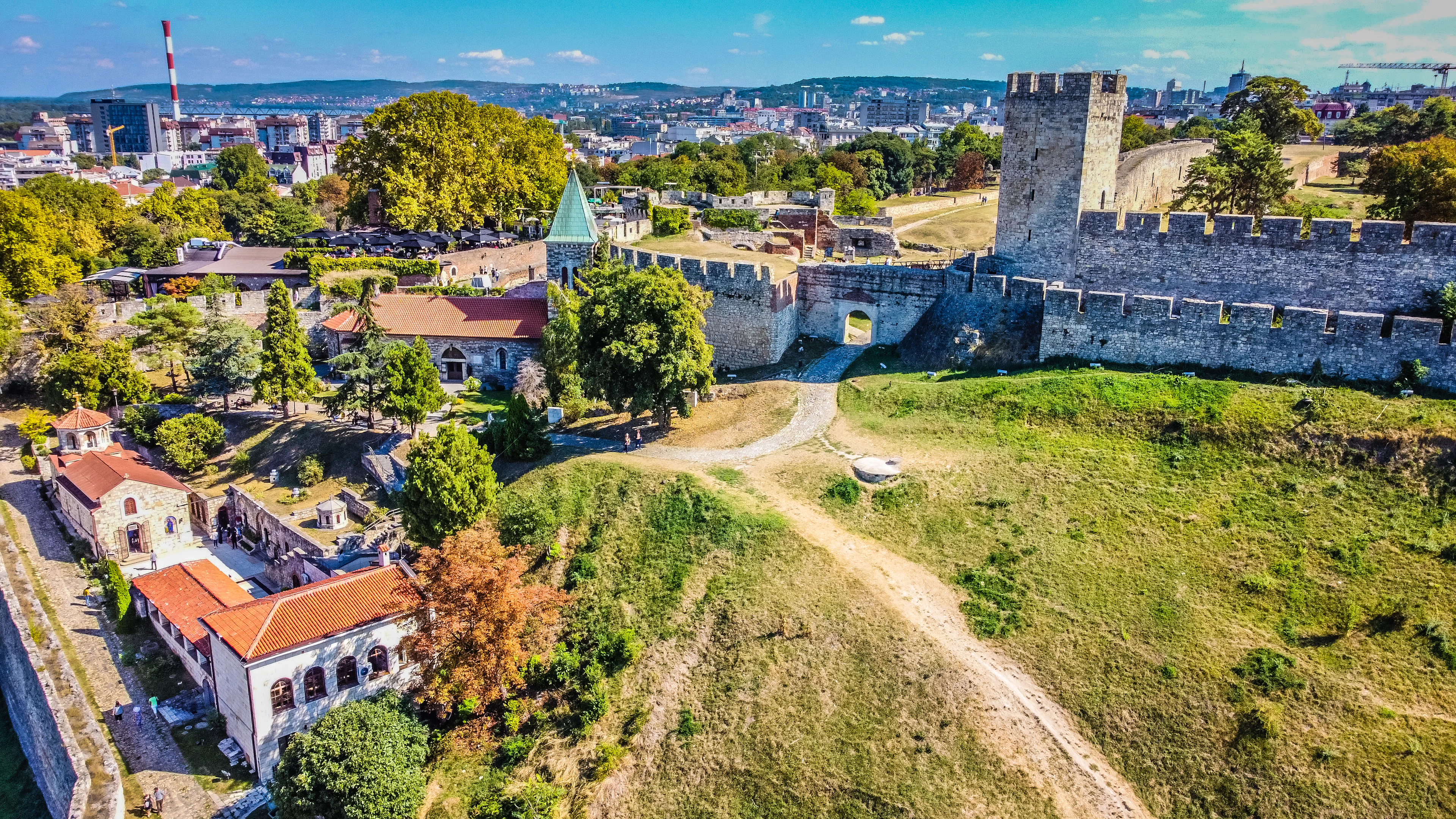 Aerial view of the ramparts, towers and green slopes of Belgrade Fortress at Kalemegdan, with the city skyline behind