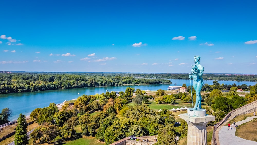 uma estátua de uma mulher em pé no topo de uma colina ao lado de um rio