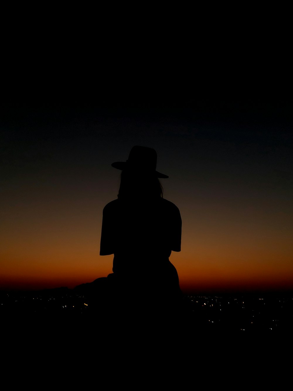 a silhouette of a person wearing a hat at sunset