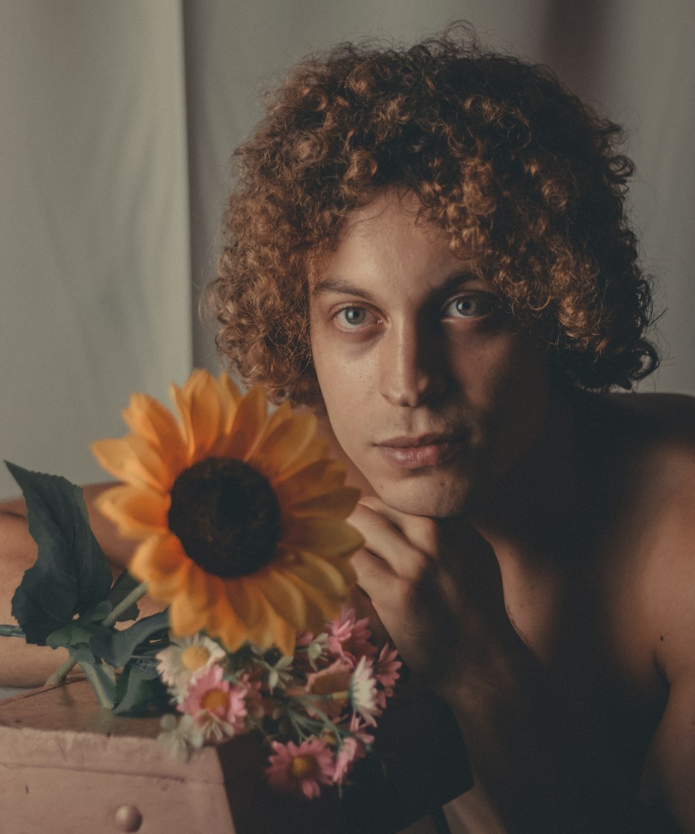 a woman with curly hair holding a sunflower