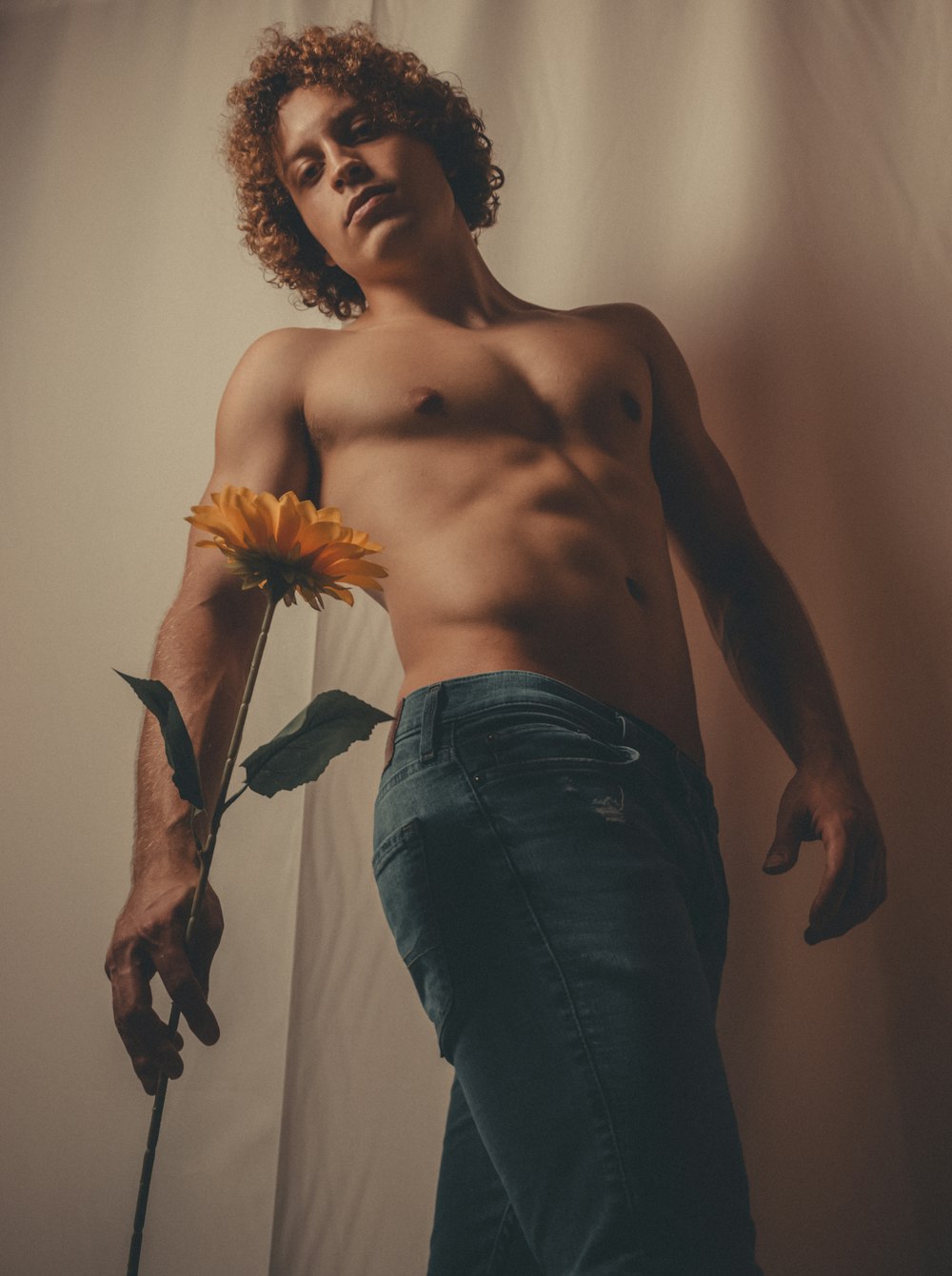 a shirtless man holding a flower in front of a curtain