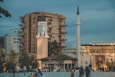 a group of people walking around a plaza with a clock tower in the background