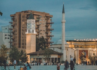 a group of people walking around a plaza with a clock tower in the background