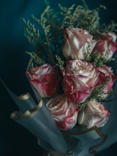 Elegant bouquet of pink roses wrapped in black and rose gold paper on a marble table.