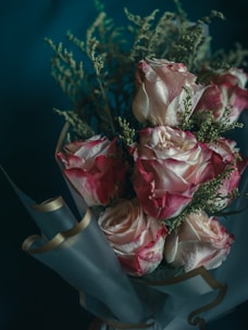 Elegant bouquet of pink roses wrapped in black and rose gold paper on a marble table.