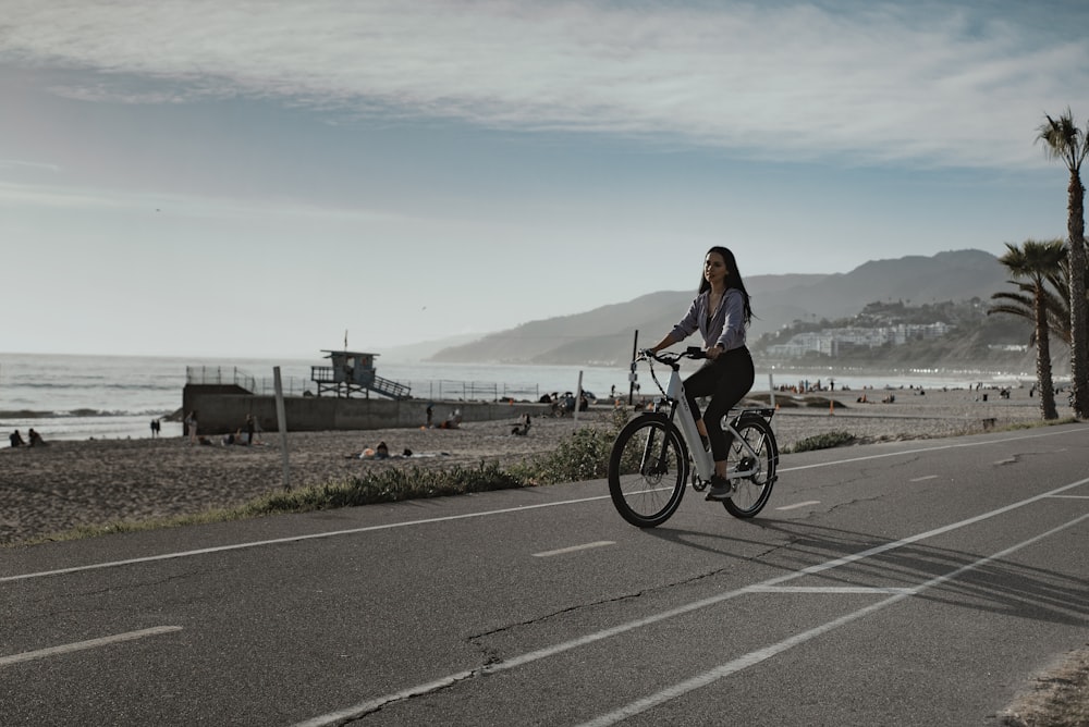 a woman riding a bike down a street next to the ocean