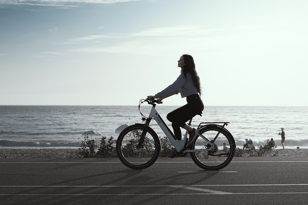 a woman riding a bike down a street next to the ocean