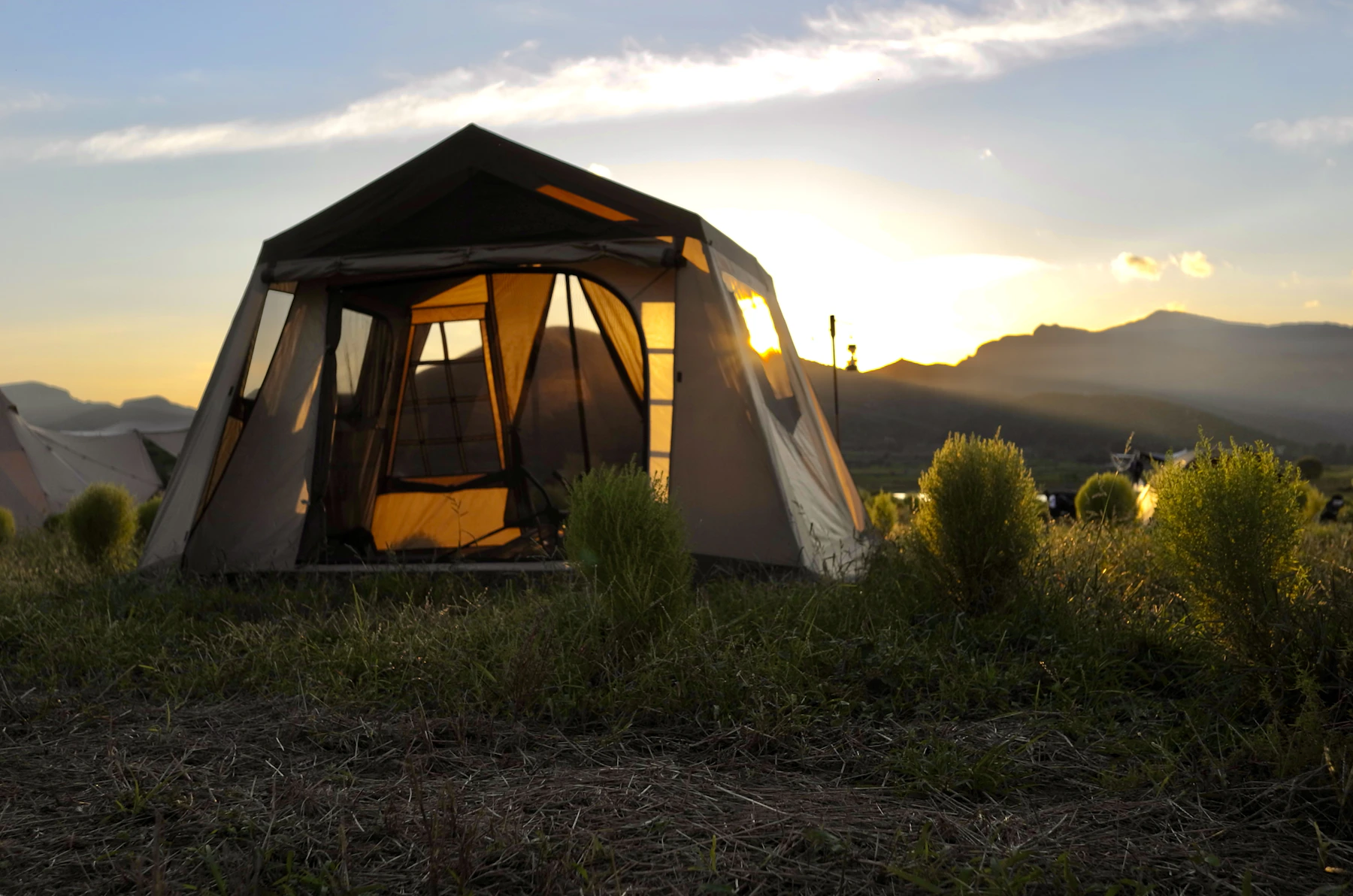 Large camping tent set up in an open outdoor landscape at sunset