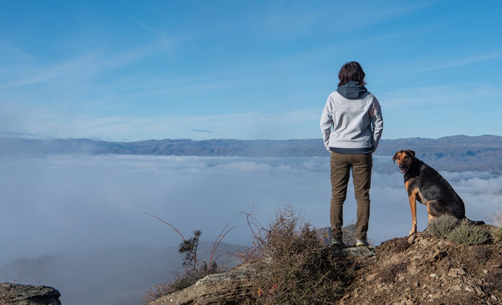 a woman standing on top of a mountain with a dog