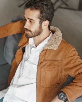 a man sitting on a couch wearing a brown jacket