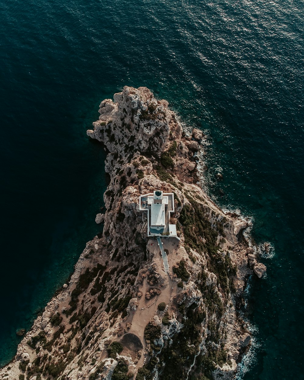 an aerial view of a house on a rocky island in the middle of the ocean
