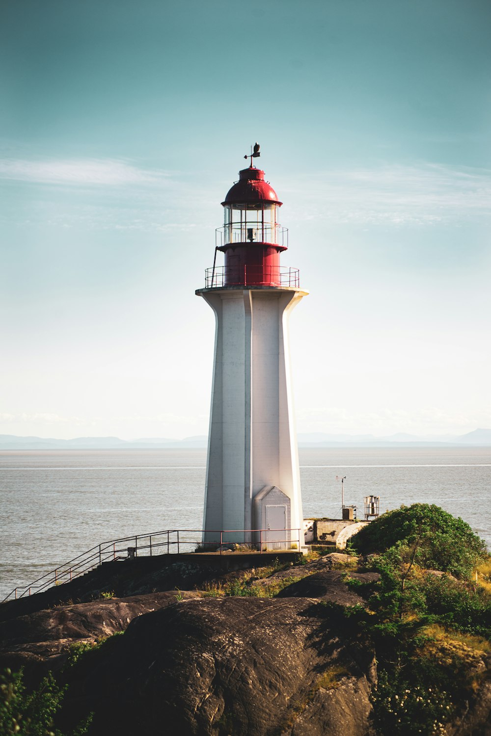 um farol branco e vermelho sentado no topo de um penhasco